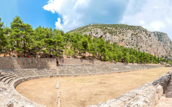 Stadium of Delphi with stone seating and surrounding trees under a clear sky.