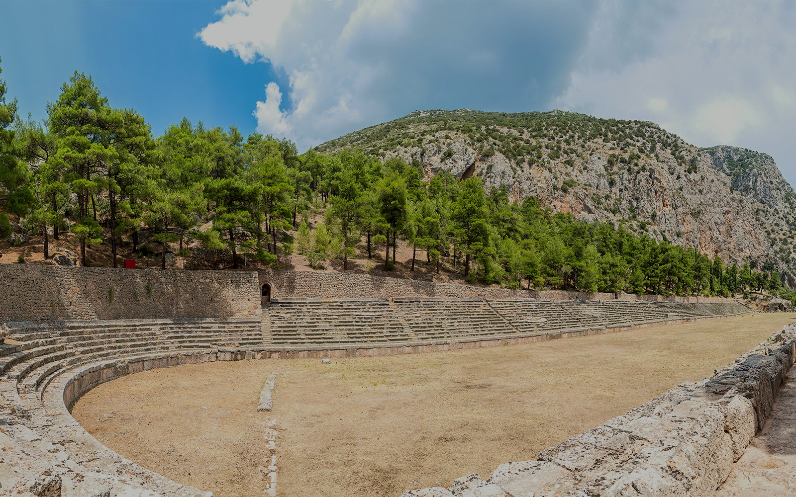 Stadium of Delphi with stone seating and surrounding trees under a clear sky.