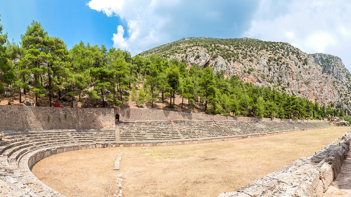 Stadium of Delphi with stone seating and surrounding trees under a clear sky.