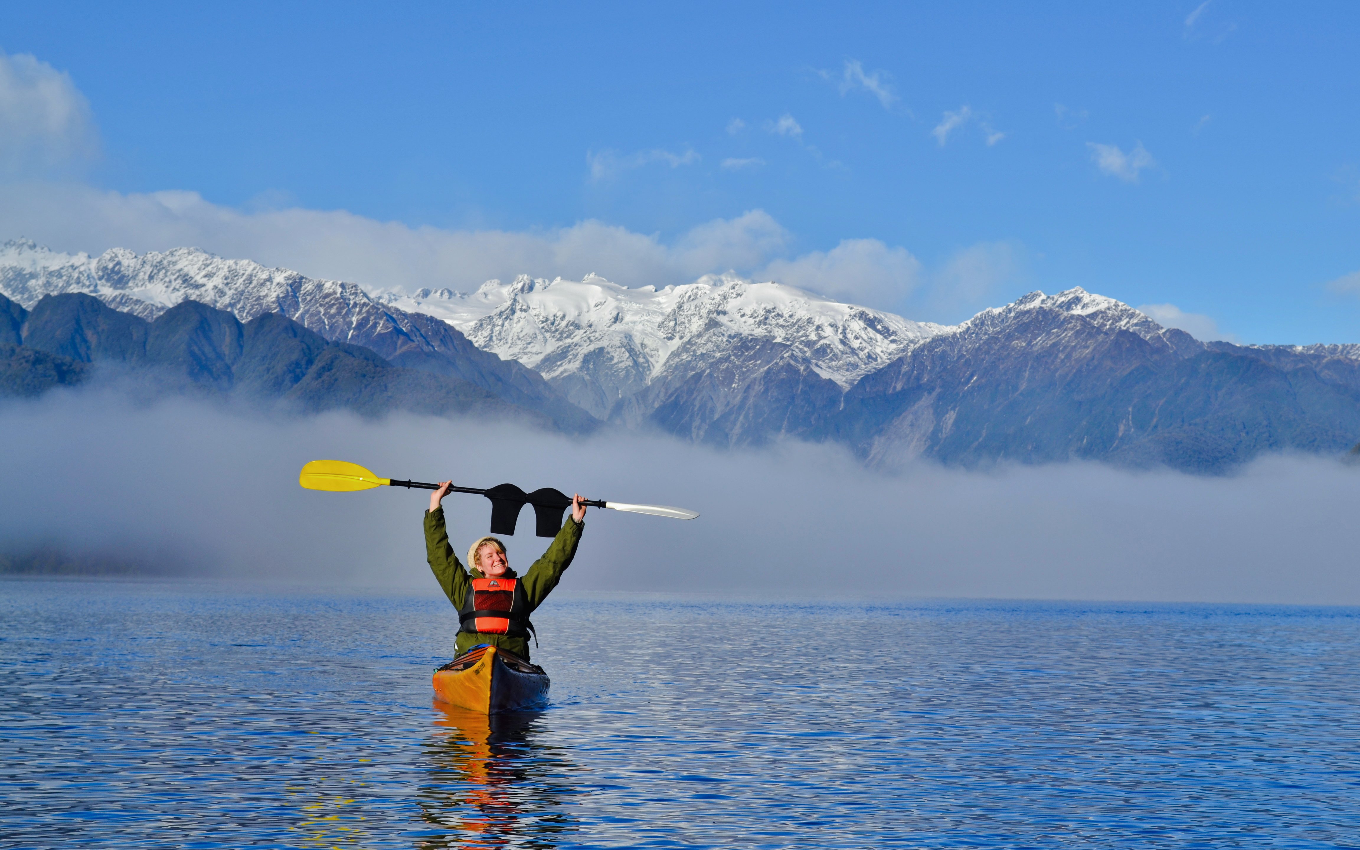 Girl kayaking on Lake Mapourika with snow-capped mountains in the background.