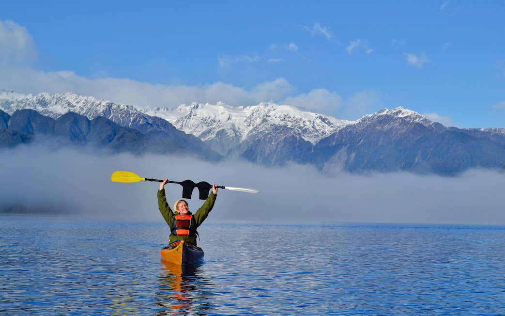 Girl kayaking on Lake Mapourika with snow-capped mountains in the background.
