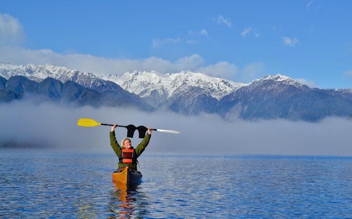 Girl kayaking on Lake Mapourika with snow-capped mountains in the background.