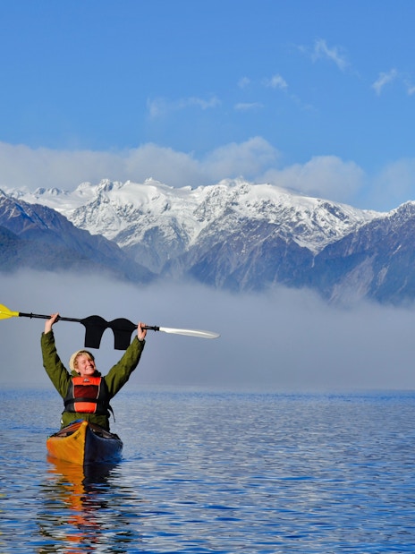 Girl kayaking on Lake Mapourika with snow-capped mountains in the background.