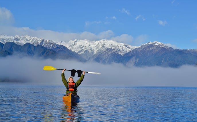 Girl kayaking on Lake Mapourika with snow-capped mountains in the background.
