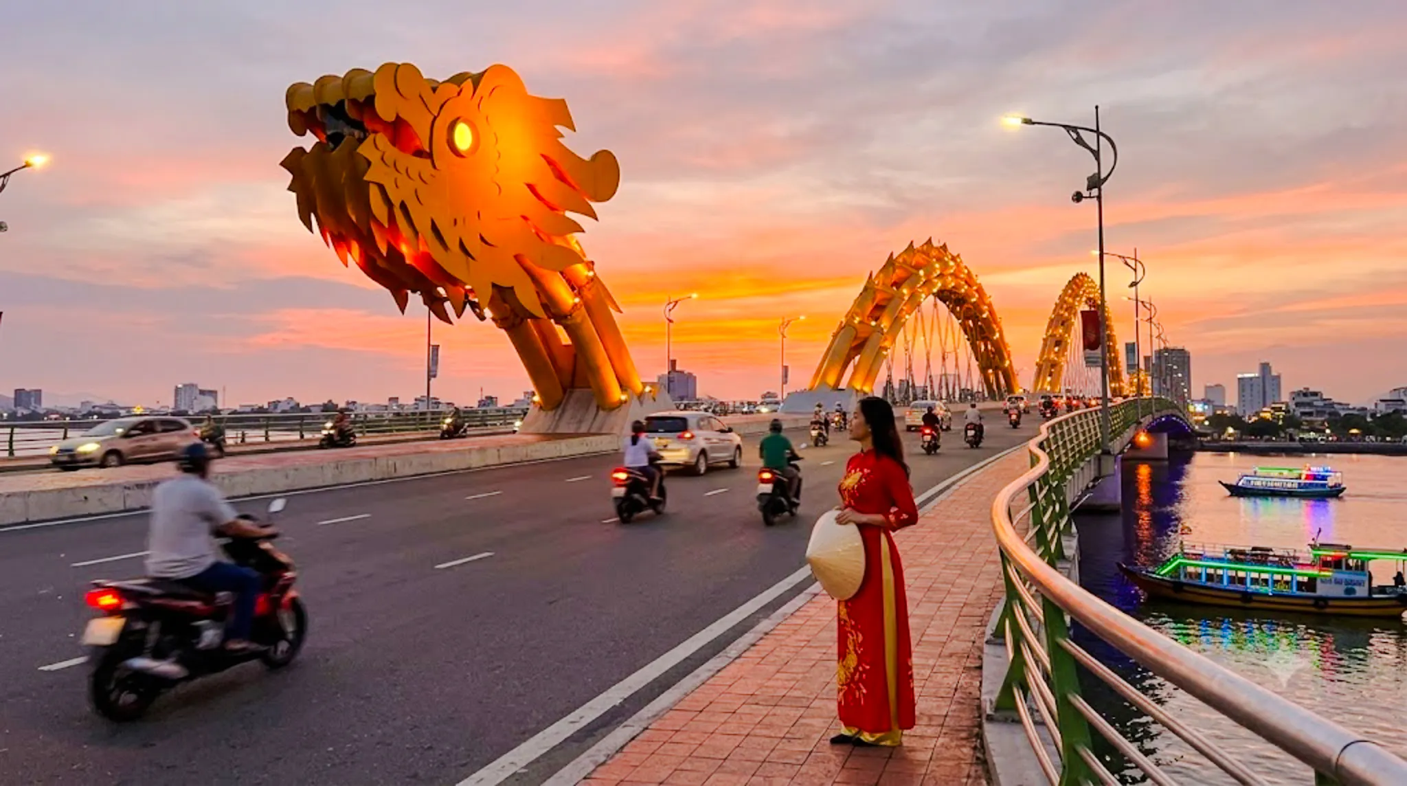 Dragon Bridge at sunset with motorbikes and a woman in traditional dress, Da Nang.