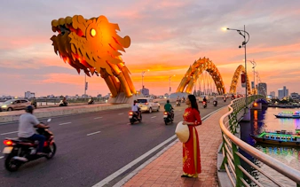 Dragon Bridge at sunset with motorbikes and a woman in traditional dress, Da Nang.
