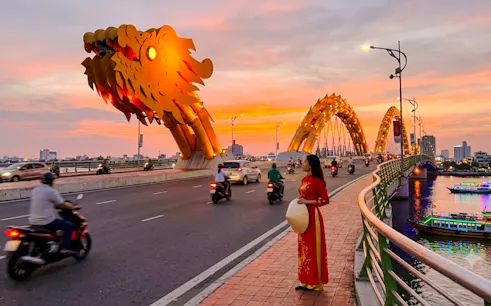 Dragon Bridge at sunset with motorbikes and a woman in traditional dress, Da Nang.
