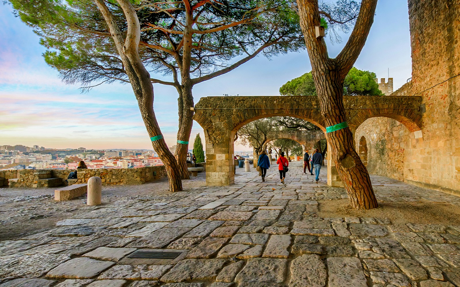 Visitors on terrace of São Jorge Castle overlooking Alfama and Baixa districts in Lisbon at sunset.