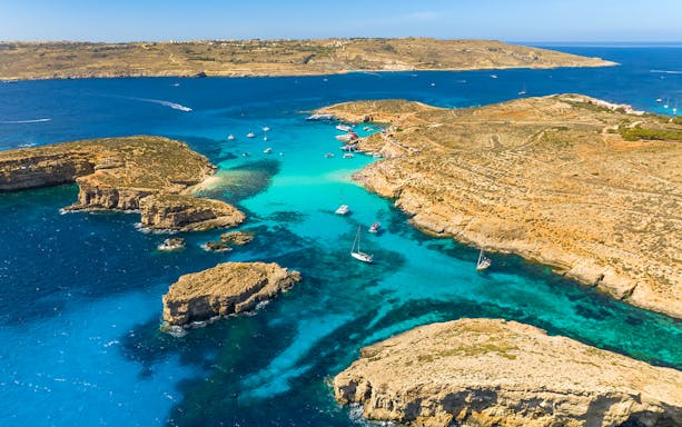 Blue lagoon on Comino Island with boats in turquoise water and rocky coastline.