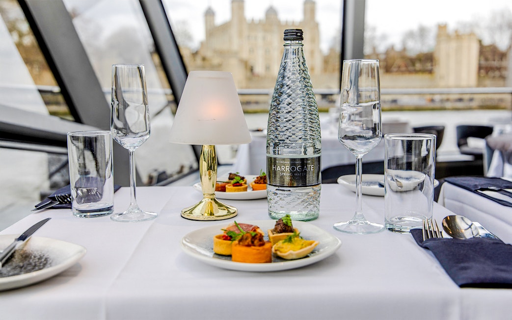Dinner table setup on Thames River cruise with appetizers and water bottle.