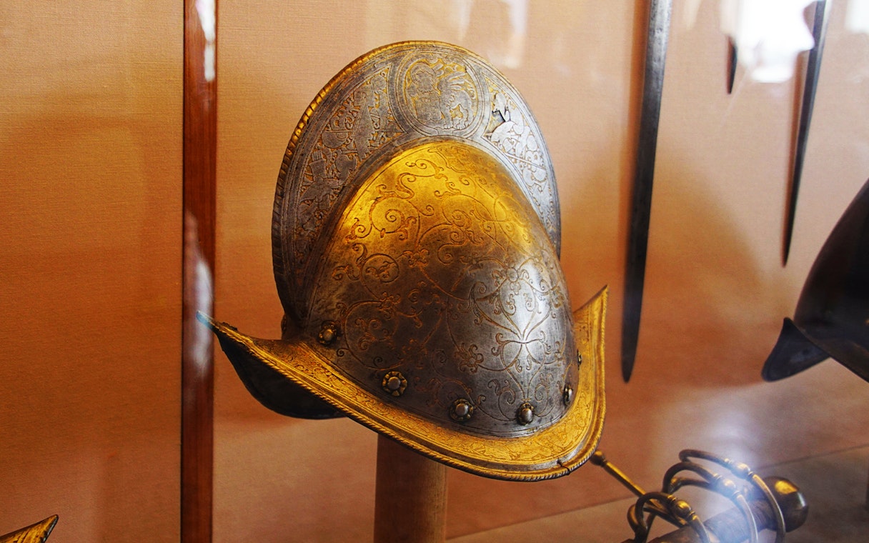 Historical helmet in Doge's Palace armory, Venice, with intricate engravings.