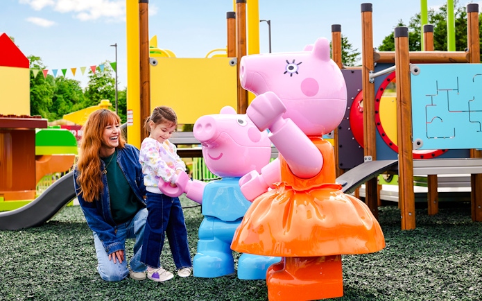 Child interacting with Peppa Pig statues at Legoland New York playground.