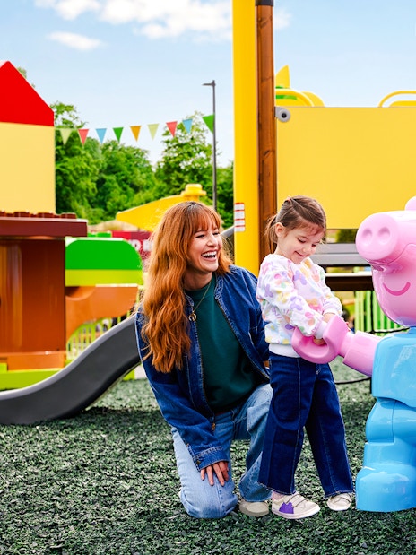 Child interacting with Peppa Pig statues at Legoland New York playground.
