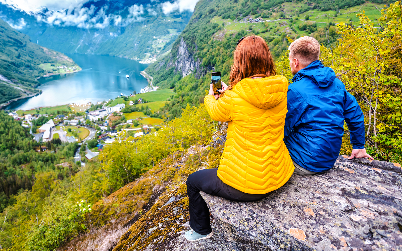 Couple overlooking Geirangerfjord from a cliff in Geiranger, Norway.