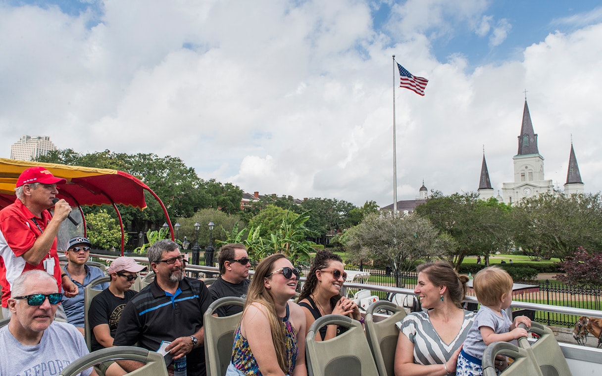 Tourists on a hop-on hop-off bus in New Orleans with St. Louis Cathedral in the background.