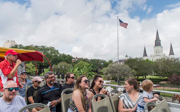 Tourists on a hop-on hop-off bus in New Orleans with St. Louis Cathedral in the background.