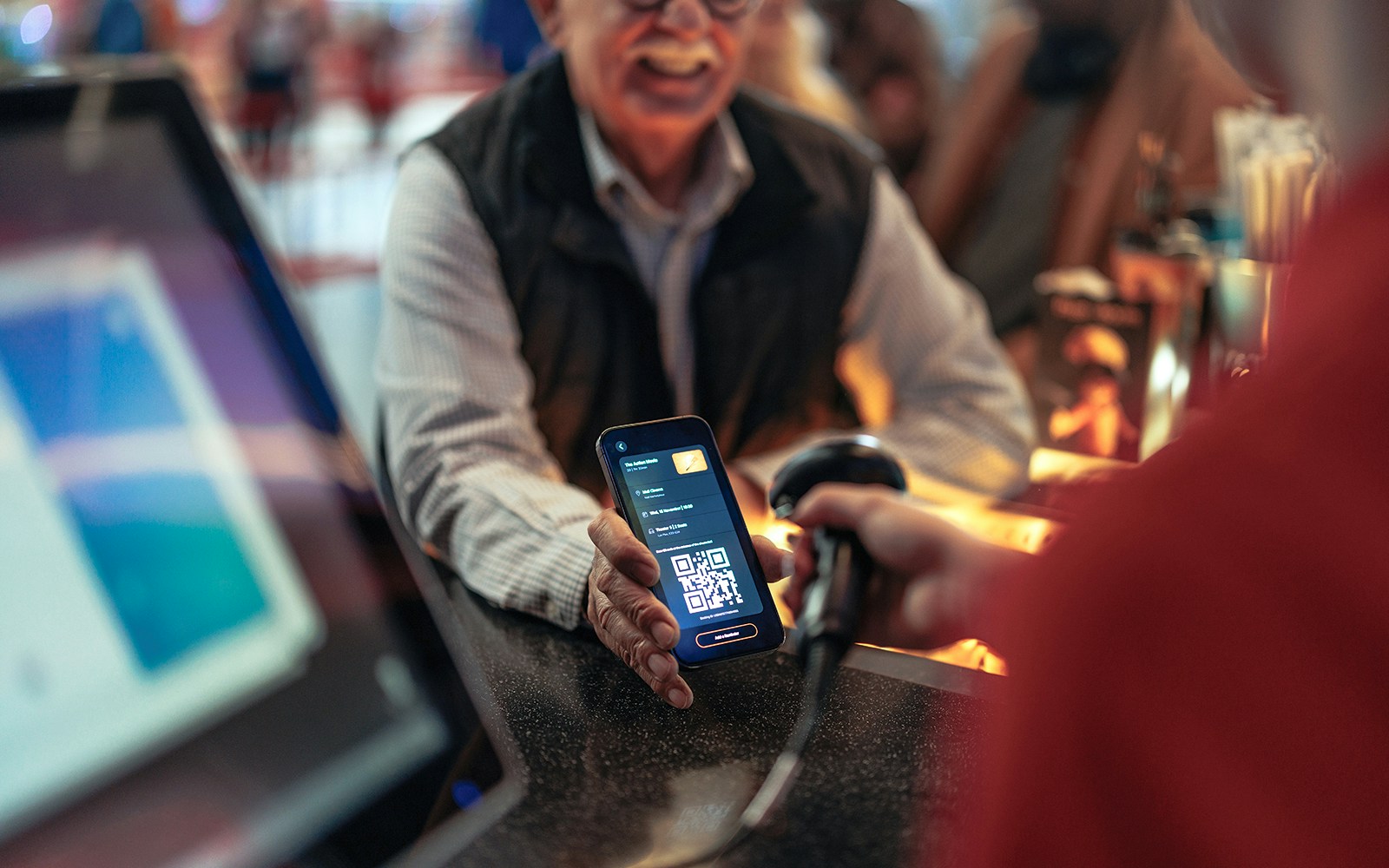 Person holding phone with QR code being scanned at a counter.