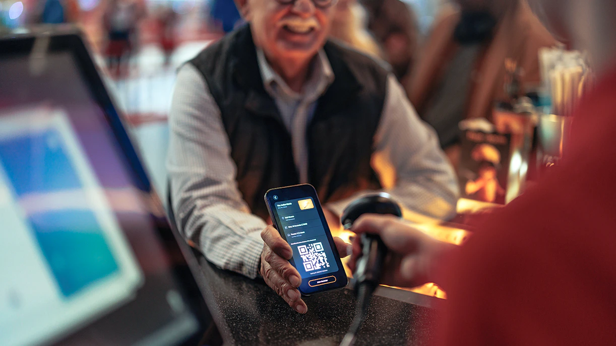 Person holding phone with QR code being scanned at a counter.