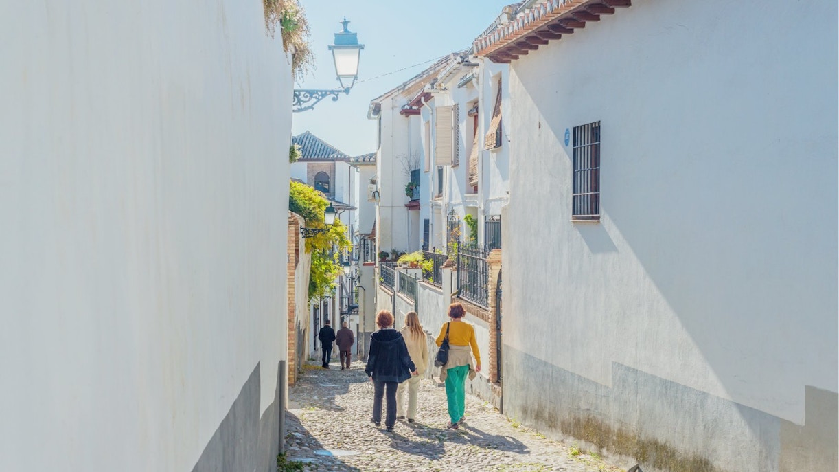 Cobbled street in Barrio Albaicin, Granada, Spain with people walking between whitewashed buildings.