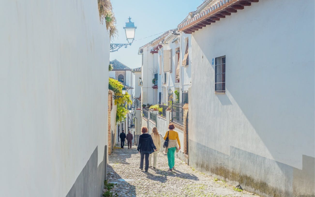 Cobbled street in Barrio Albaicin, Granada, Spain with people walking between whitewashed buildings.