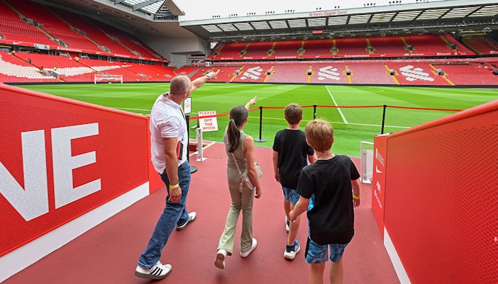 Visitors touring Anfield Stadium, home of Liverpool FC, with a guide pointing at the field.