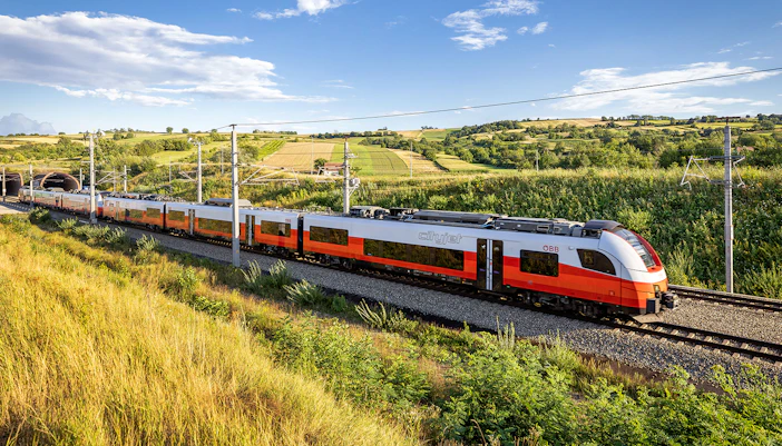 Train traveling through scenic countryside with rolling hills in the background.