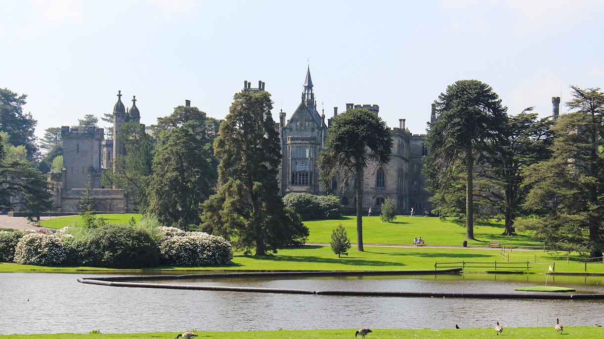 Exteriors of Alton Towers with lush gardens and a serene pond in the foreground.