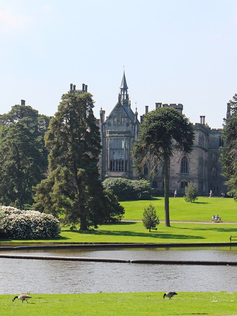 Exteriors of Alton Towers with lush gardens and a serene pond in the foreground.