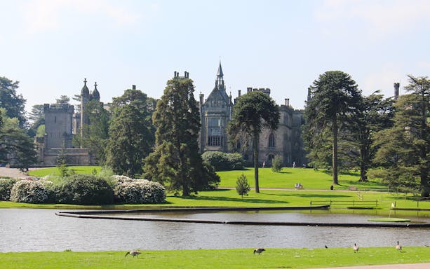 Exteriors of Alton Towers with lush gardens and a serene pond in the foreground.