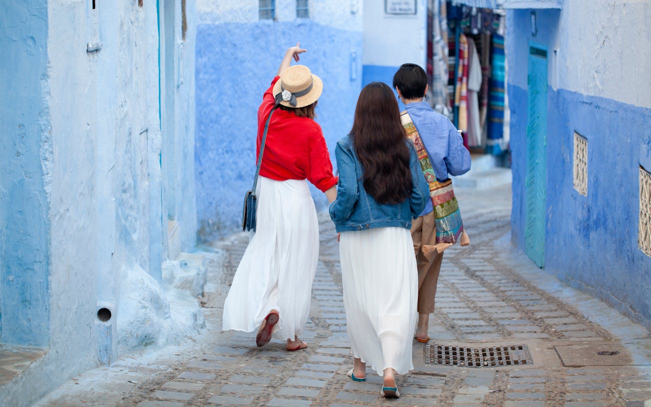 Tourists walking with guide in blue streets of Chefchaouen, Morocco.