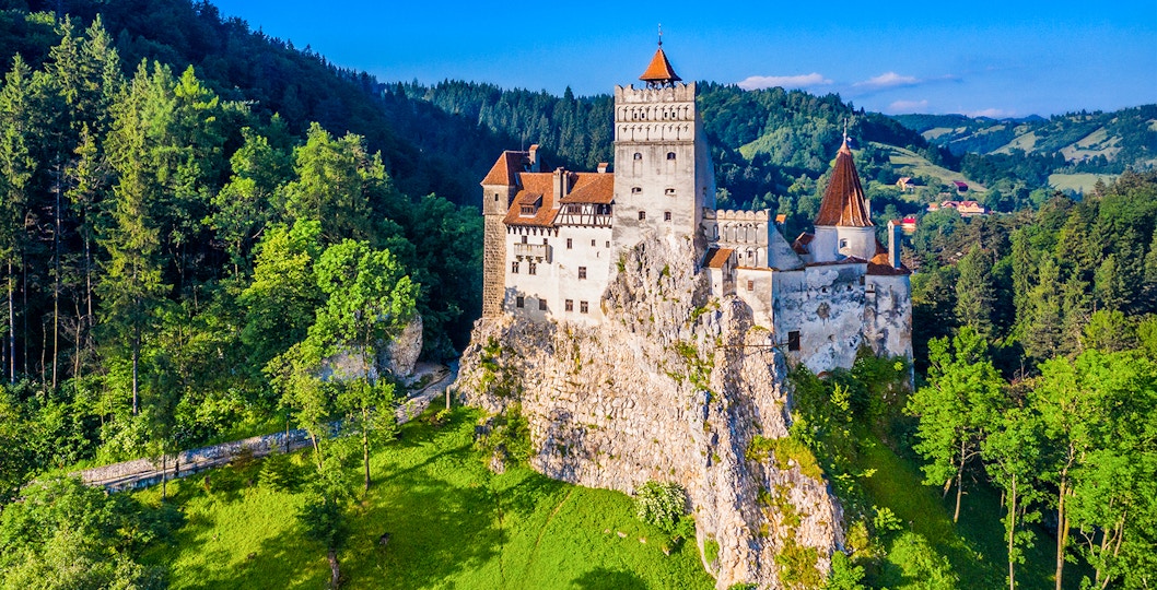 Bran Castle in Romania surrounded by lush green forest and rocky landscape.