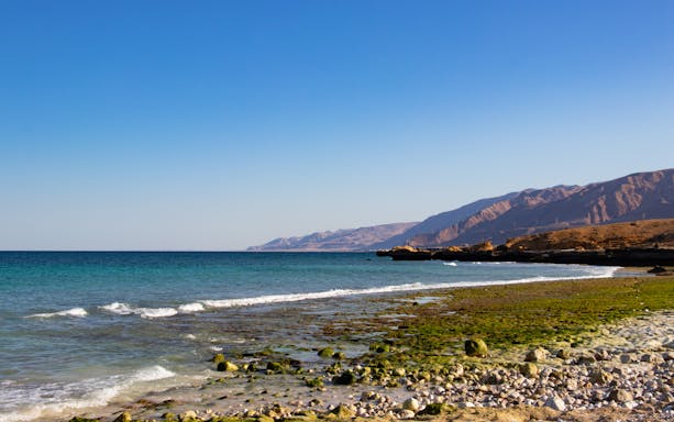 Fins Beach shoreline with rocky terrain and distant mountains near Muscat, Oman.