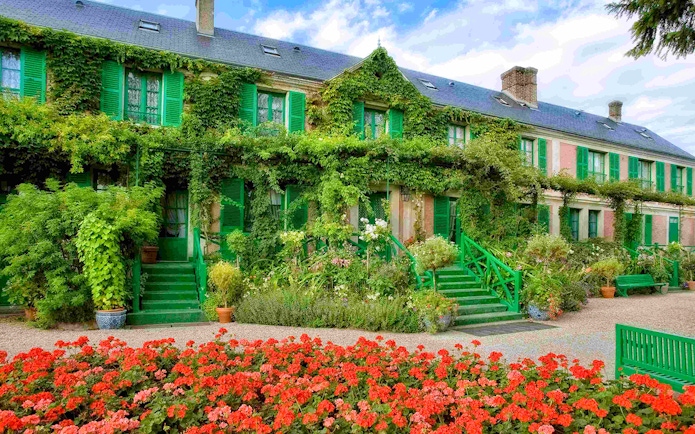 Giverny Gardens with vibrant flowers and ivy-covered house, part of Versailles Palace & Giverny tour.