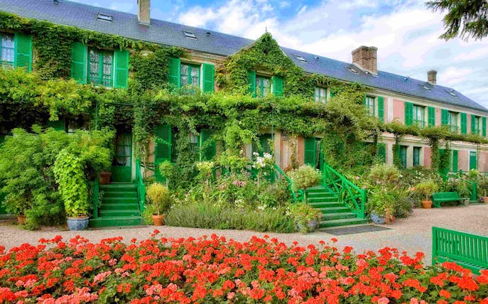 Giverny Gardens with vibrant flowers and ivy-covered house, part of Versailles Palace & Giverny tour.