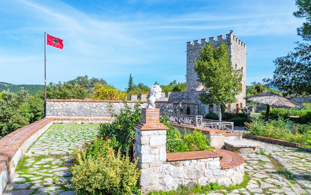Historic stone tower and Albanian flag in Butrint National Park, Saranda City.