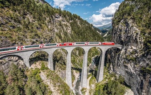 Glacier Express crossing the Landwasser Viaduct in Graubünden, surrounded by forested mountains.