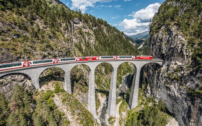 Glacier Express crossing the Landwasser Viaduct in Graubünden, surrounded by forested mountains.