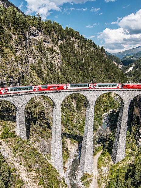 Glacier Express crossing the Landwasser Viaduct in Graubünden, surrounded by forested mountains.