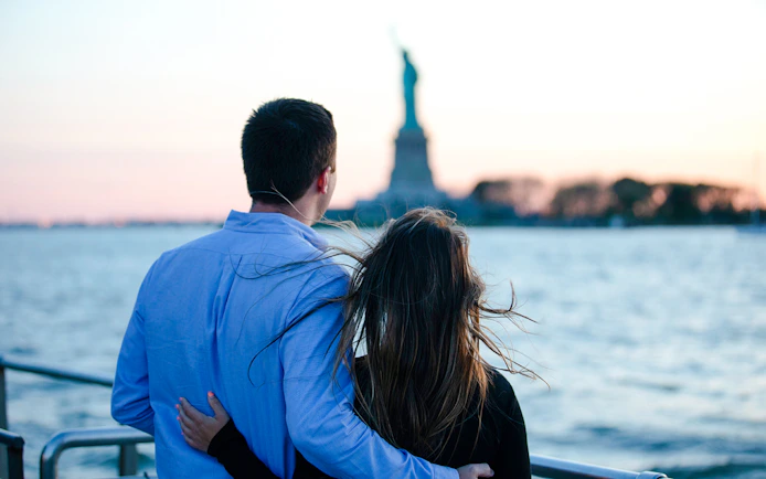 Couple enjoying sunset view of Statue of Liberty on luxury glass boat cruise.