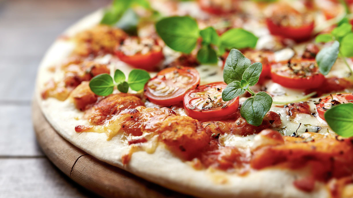 Close-up of a pizza with tomatoes, cheese, and fresh basil leaves.