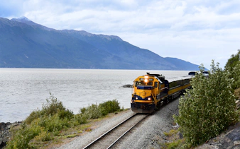Train on Alaska Railroad by scenic mountain lake.
