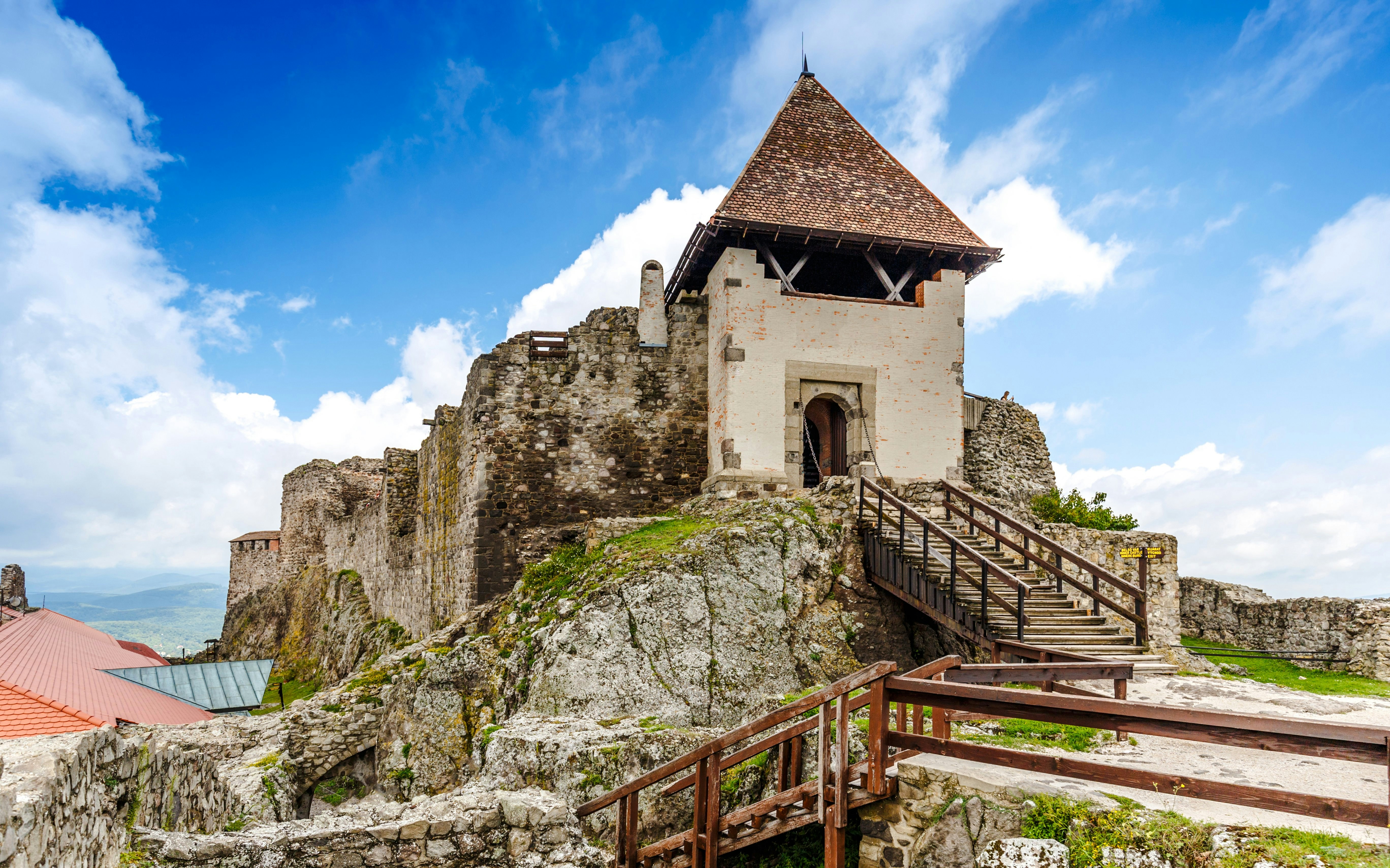 Visegrad Castle with stone walls and wooden stairs under a blue sky.