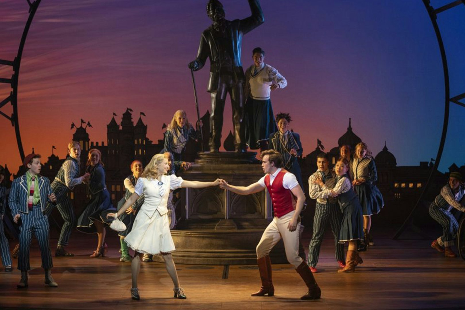 Cast performing a scene from Wicked the Musical on stage with a statue backdrop.