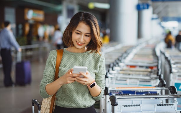 Woman using phone near luggage carts at Tirana airport.