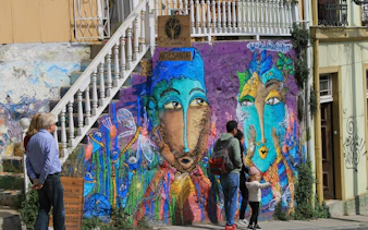 Tourists admire colorful mural on building wall near white staircase in Cerro Alegre, Valparaíso.