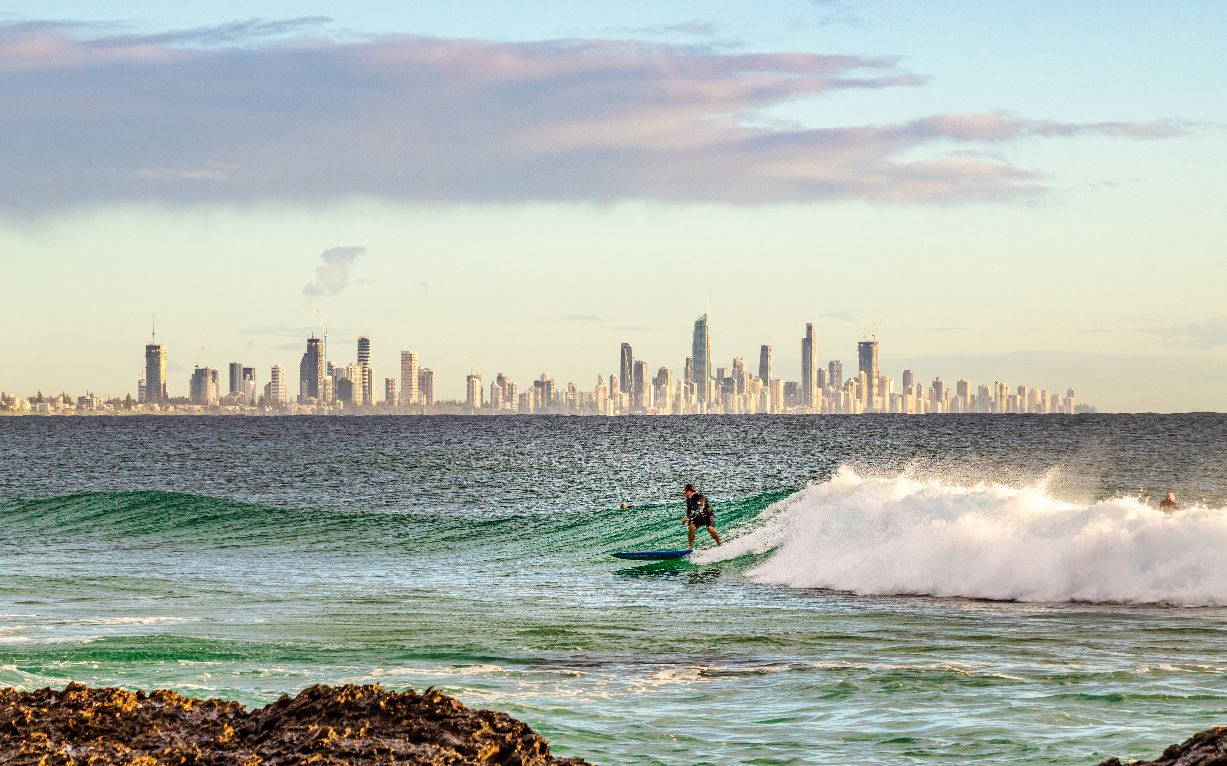 Surfista su un'onda a Burleigh Head con lo skyline della Gold Coast sullo sfondo.