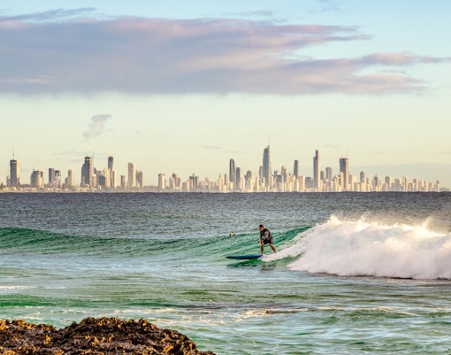 Surfista su un'onda a Burleigh Head con lo skyline della Gold Coast sullo sfondo.
