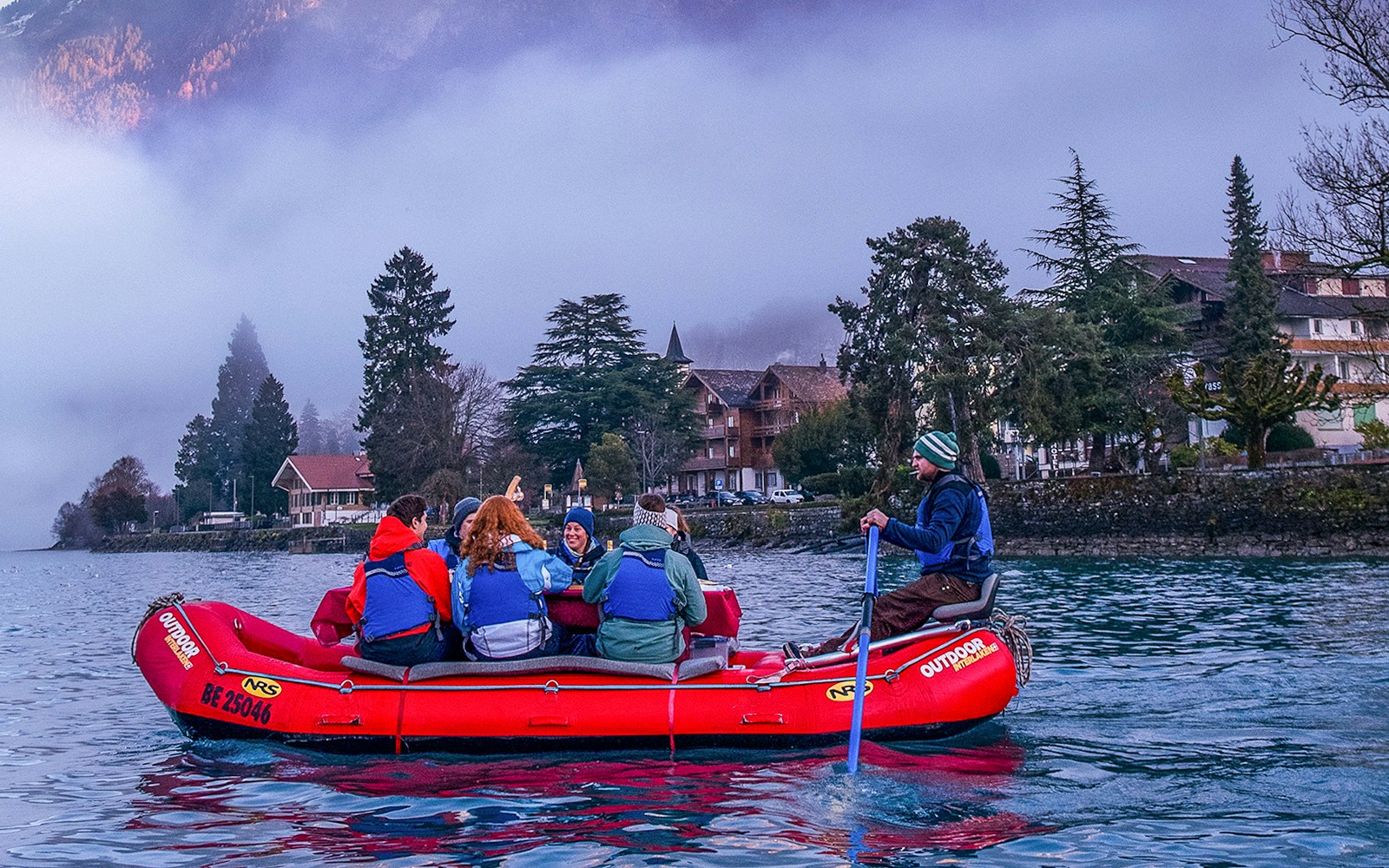 River rafting group on a lake in Interlaken with misty mountains and trees in the background.