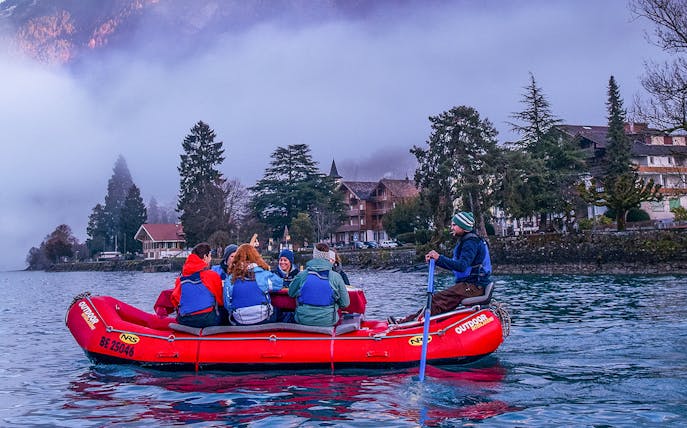 River rafting group on a lake in Interlaken with misty mountains and trees in the background.