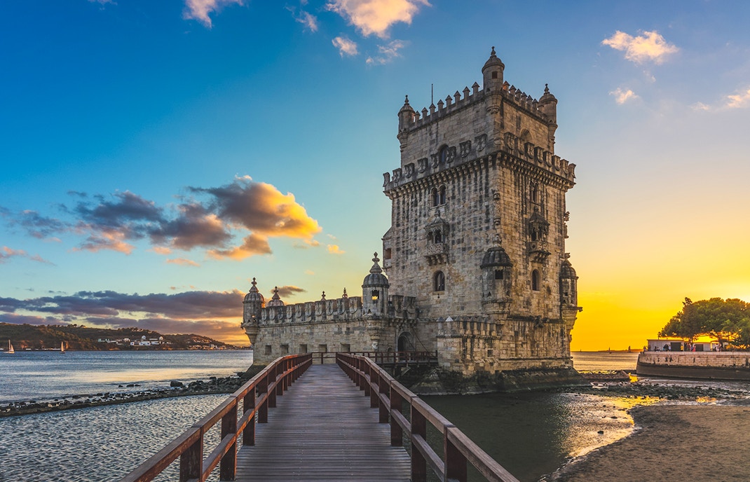 Belem Tower in Lisbon silhouetted against a vibrant sunset sky.